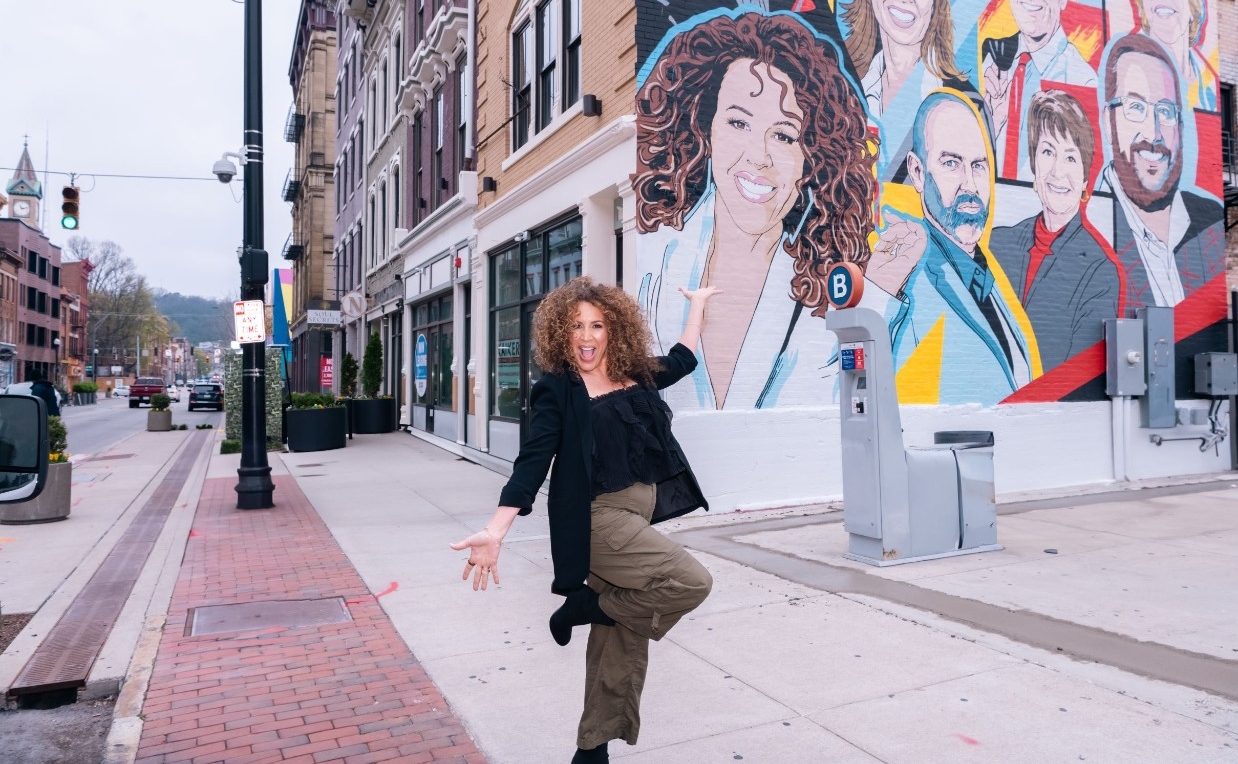 Diana Maria Riva posing in front of her portrait on the 2025 Alumni Celebration Mural