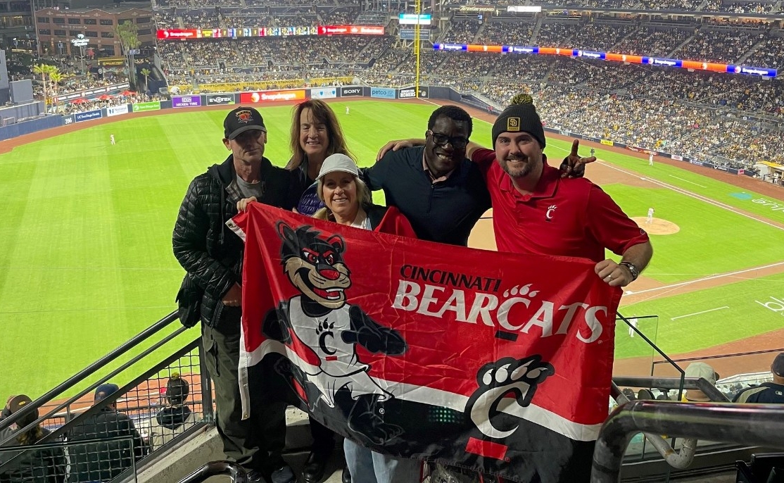 alumni at a baseball game holding a UC flag