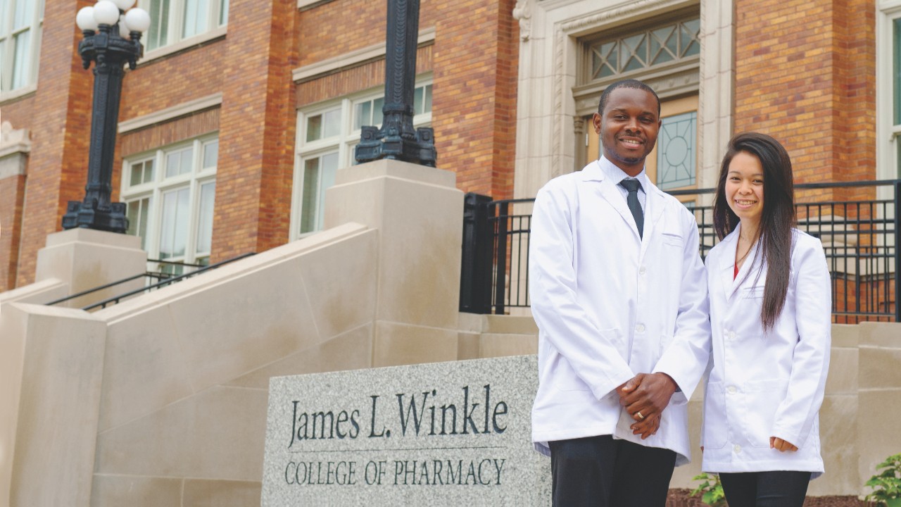 Man and woman stand in front of James L. Winkle College of Pharmacy sign