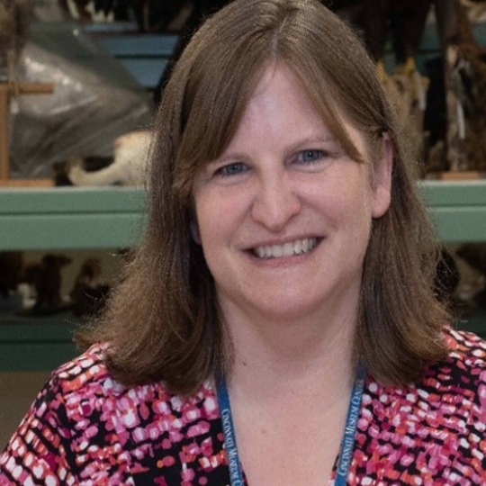 Alumna Nicole Wiesmann sits on a couch smiling