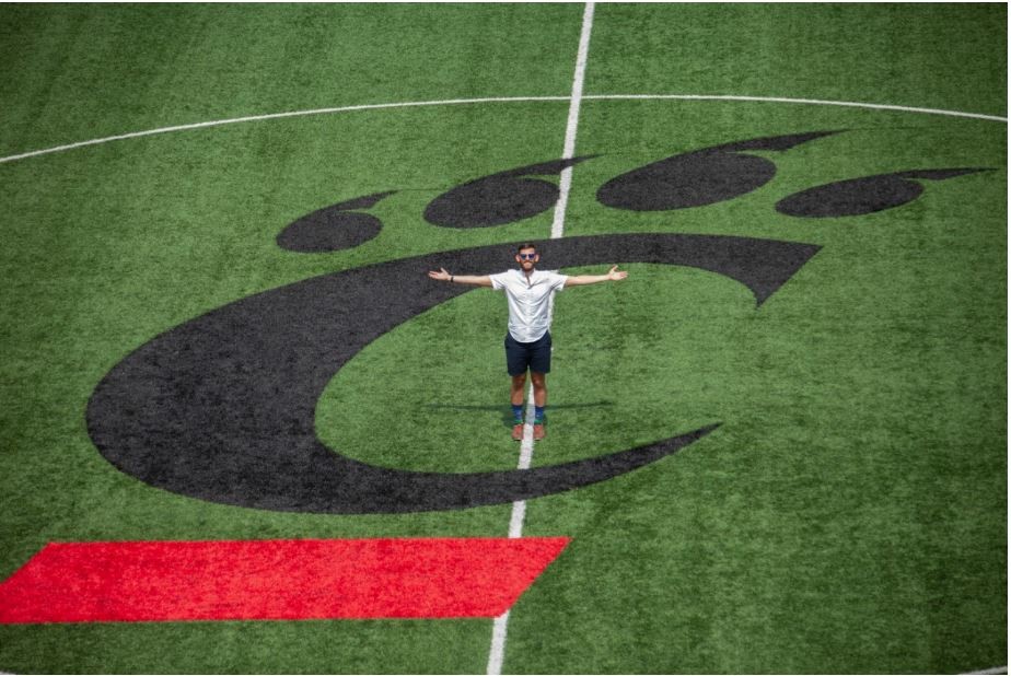 Man stands in center of UC soccer field with arms wide