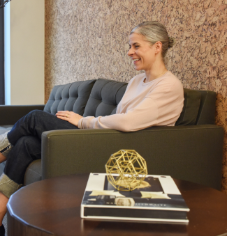 Alumna Nicole Wiesmann sits on a couch smiling